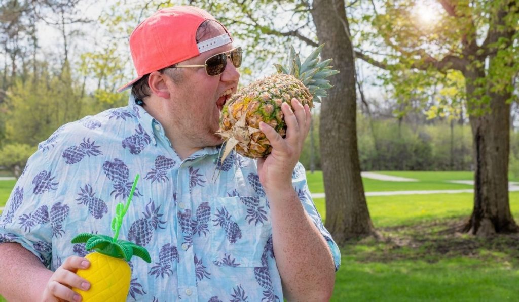 big man pretending to take a bite of fresh pineapple - ee220321