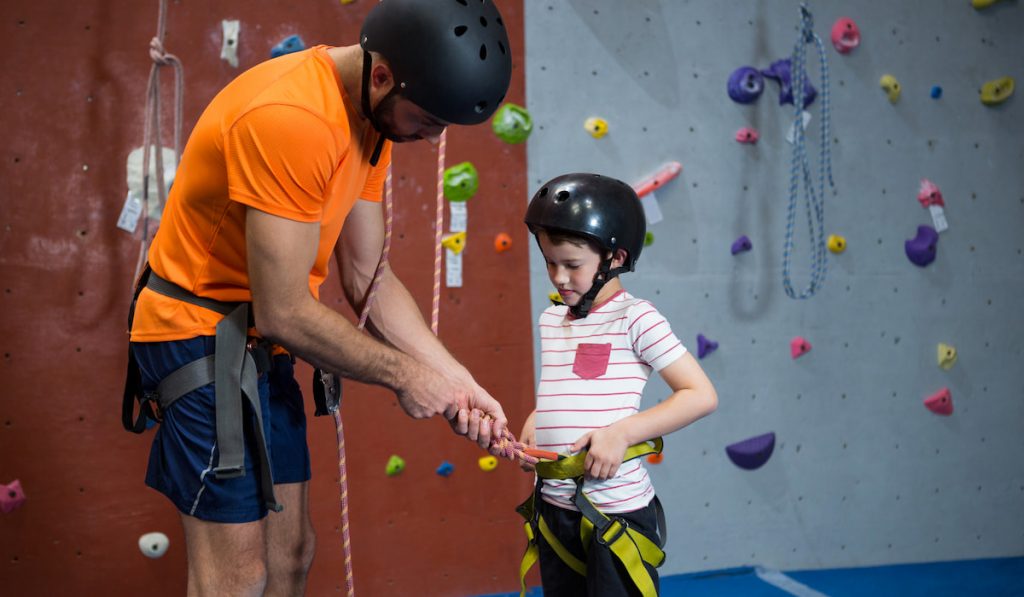 trainer assisting cute little boy to wear safety harness 