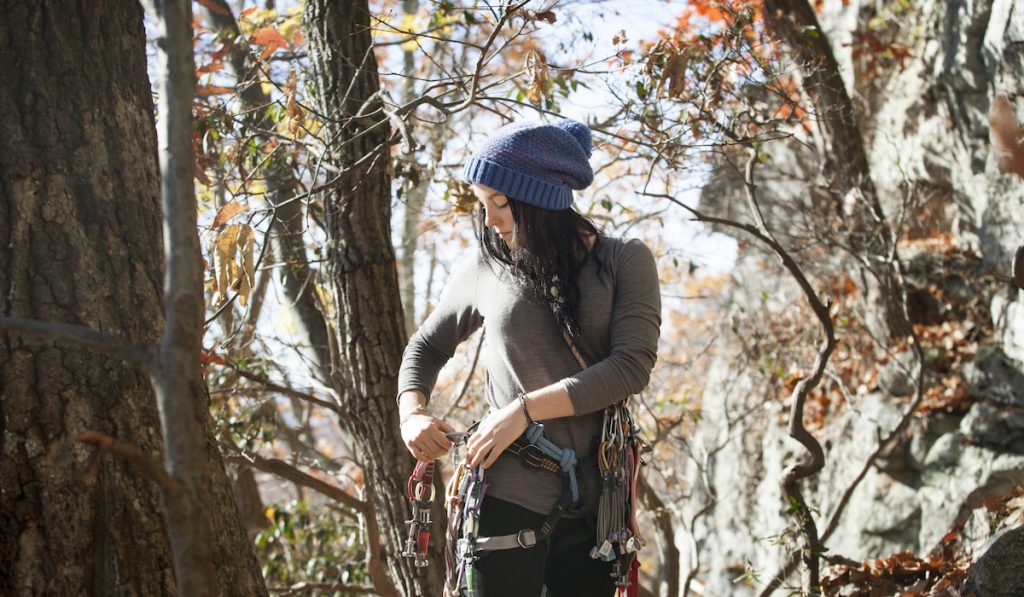 woman adjusting safety harness while standing by trees